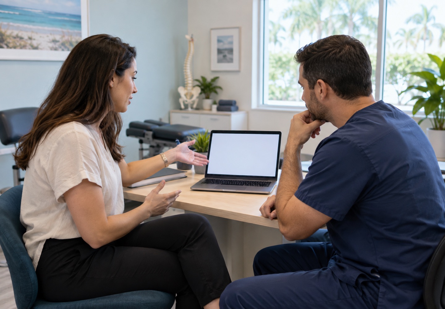 An adult describing their desk setup to a clinician using a laptop with a blank screen.